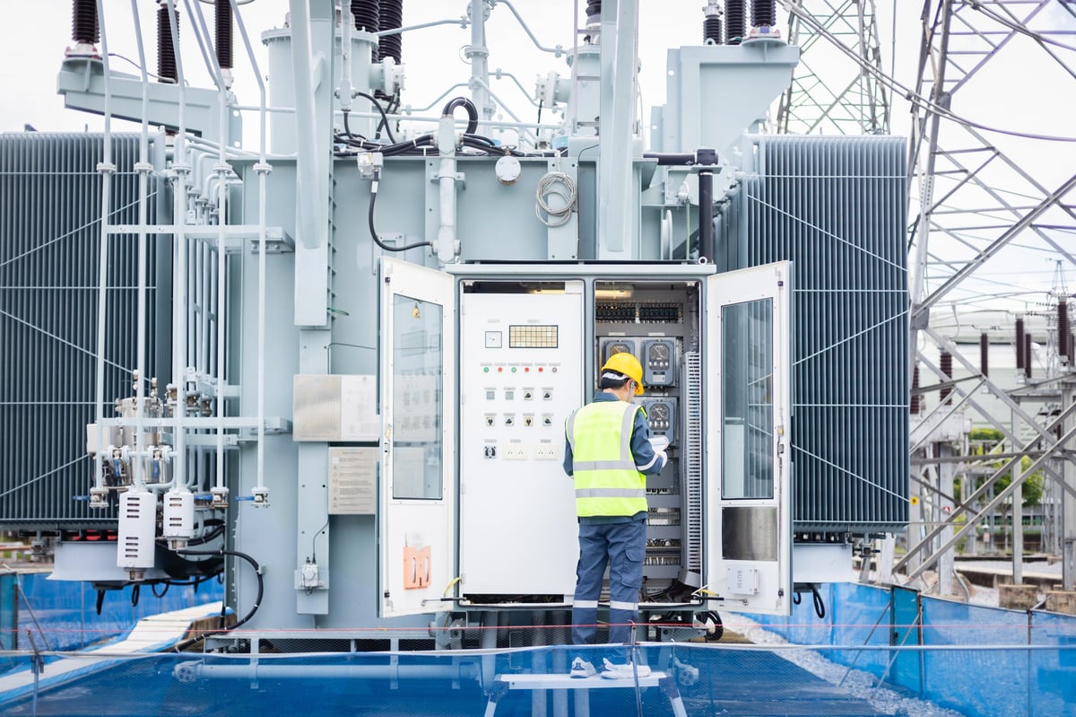 Ingeniero trabajando en subestación de alta tensión realizando inspección de infraestructura eléctrica