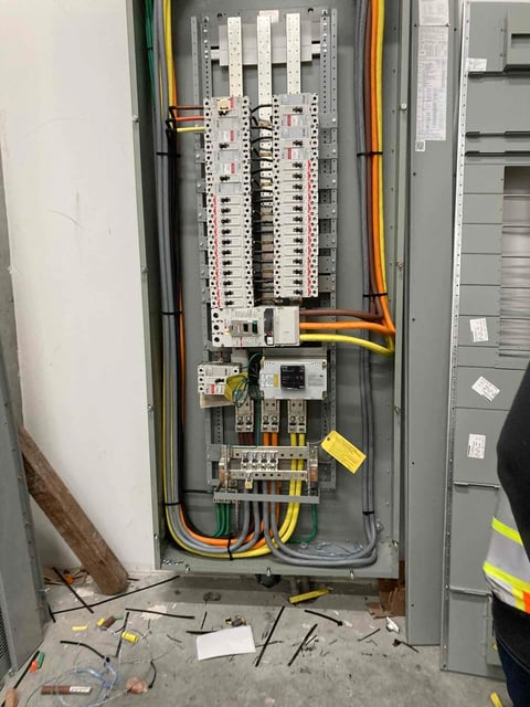 Interior of electrical panel showing circuit breakers, wiring, and colored cables in an open metal cabinet