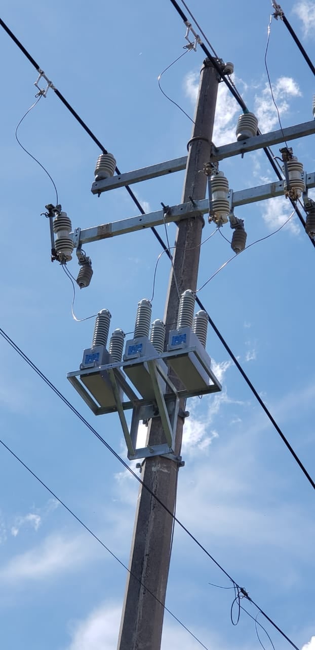 Electrical utility pole with multiple insulators, transformers, and power lines against a blue sky with clouds