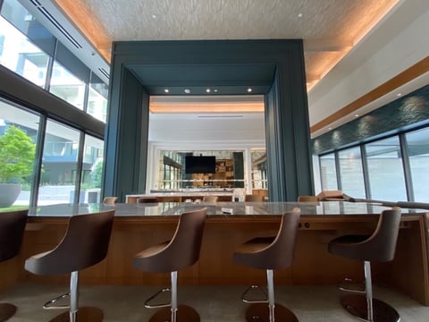Modern minimalist cafe interior with brown leather bar stools facing a counter, framed by dark doorway with warm ceiling lighting.