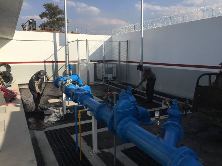 Sistema de tubería de agua industrial azul montado sobre plataforma de concreto con estructura metálica y barricada de protección