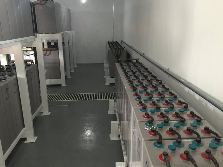 Instalación industrial con maquinaria blanca en la pared izquierda y filas de equipos coloridos dispuestos en el lado derecho a lo largo de un sistema de rieles