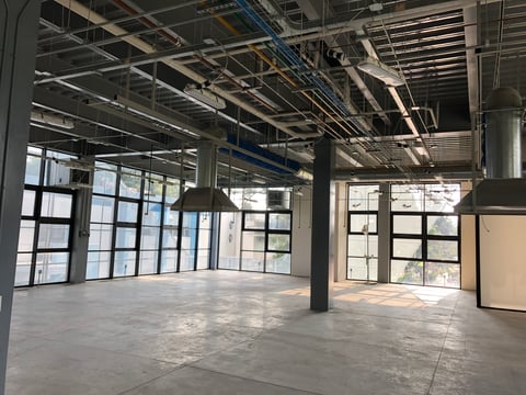 Empty industrial loft space with large windows, concrete floor, exposed ceiling beams and ductwork