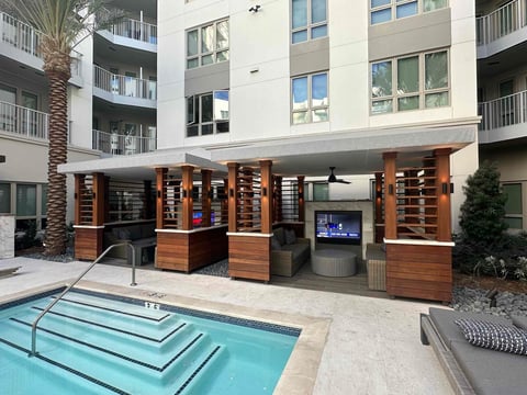 Modern apartment complex courtyard with pool, wooden pavilion structure, and multi-story residential building