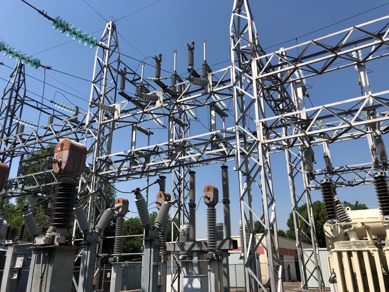 High-voltage electrical substation with metal towers, transformers, and power lines under blue sky
