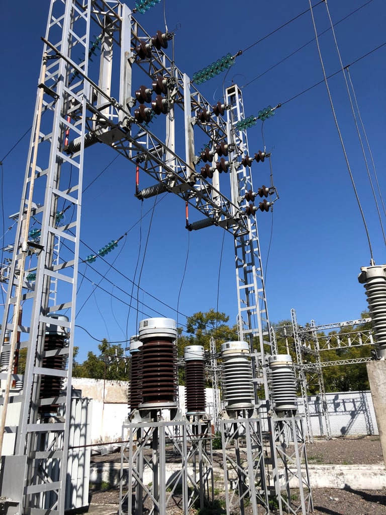 Subestación eléctrica de alta tensión con torres de transmisión blancas, múltiples aisladores y líneas eléctricas contra un cielo azul despejado