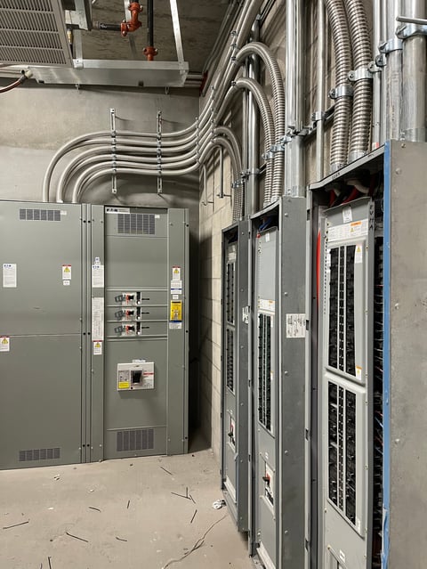 Sala de tableros eléctricos industriales con tubería conduit metálica y cableado recorriendo el techo, con múltiples gabinetes eléctricos grises y azules