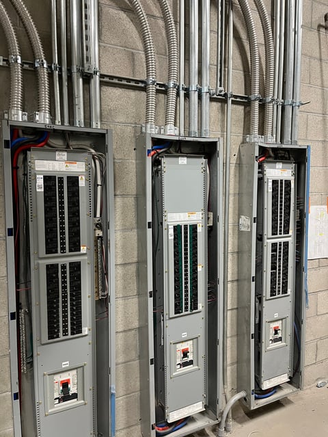 Three electrical panel boxes mounted on a concrete wall with metal conduit tubing and wiring running above them