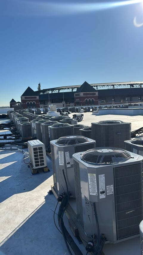 Rooftop HVAC units on industrial building with waterfront and historic structures in background under clear blue sky