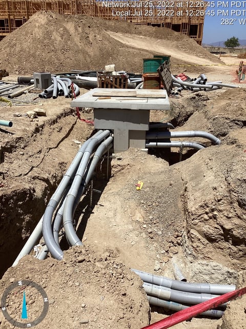 Construction site with underground drainage pipes and vault in sandy soil, scattered equipment and materials visible in background