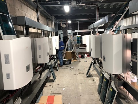 Bodega industrial con grandes equipos cilíndricos blancos y maquinaria en estanterías, bajo iluminación cenital brillante